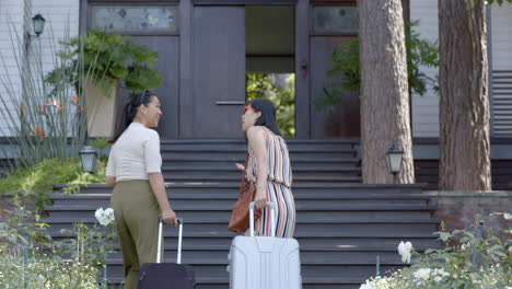 Happy-asian-female-friends-with-suitcases-walking-on-stairs-of-home-on-sunny-day,-slow-motion