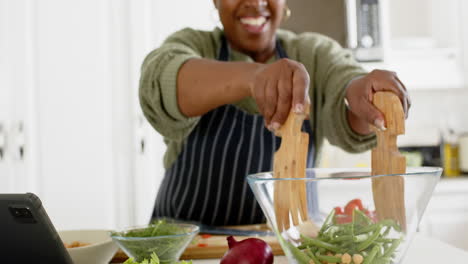 Glückliche-Afroamerikanische-Seniorin,-Die-Gemüse-Mischt-Und-In-Der-Sonnigen-Küche-Lächelt,-Zeitlupe