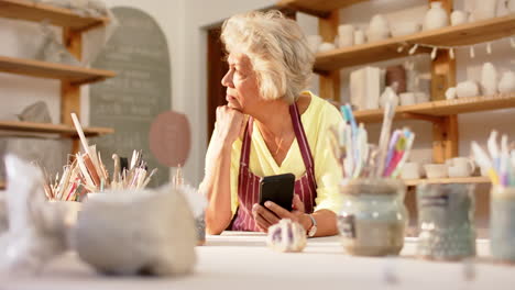 Pensive-biracial-female-potter-with-gray-hair-looking-ahead-in-pottery-studio,-slow-motion