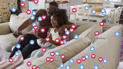 Animation-of-social-media-icons-over-african-american-father-and-daughter-watching-tv