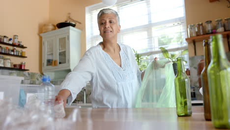 Glückliche-ältere-Frau-Mit-Gemischter-Abstammung,-Die-Zu-Hause-Plastikflaschen-Trennt,-Zeitlupe