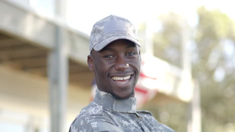 Glücklicher-Afroamerikanischer-Soldat,-Der-An-Einem-Sonnigen-Tag-Mit-Der-Flagge-Im-Hintergrund-Lacht,-Zeitlupe