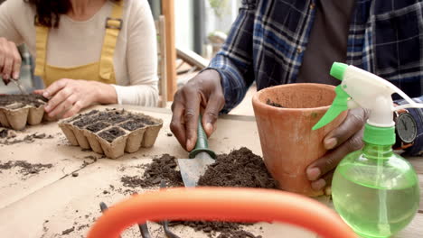 Midsection-of-diverse-mature-couple-planting-seedlings-in-pots-on-table-in-garden,-slow-motion
