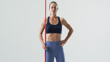 Young-Caucasian-woman-athlete-stands-confidently-holding-a-javelin-on-a-white-background