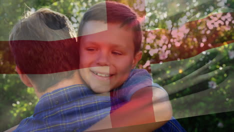 Animation-of-english-flag-over-happy-caucasian-father-and-son-embracing-in-sunny-garden