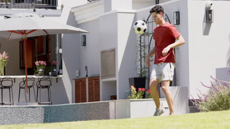Focused-biracial-man-juggling-football-with-thighs-in-sunny-garden,-copy-space,-slow-motion