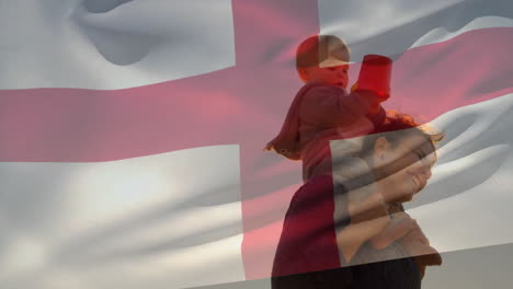 Animation-of-english-flag-over-happy-caucasian-mother-with-child-on-shoulders-on-beach