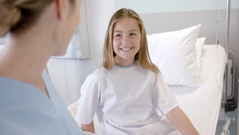 Caucasian-female-doctor-talking-with-happy-girl-patient-sitting-on-hospital-bed,-slow-motion