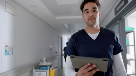 Biracial-male-doctor-using-tablet-and-walking-in-hospital-corridor,-slow-motion