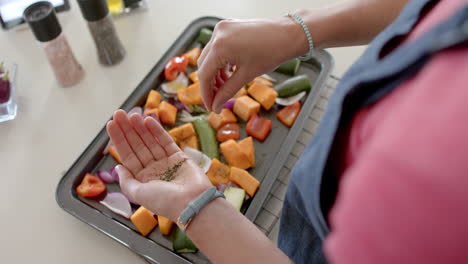 Diverse-woman-preparing-fresh-vegetables-and-seasoning-in-kitchen,-slow-motion
