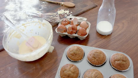 Freshly-baked-cupcakes,-mixing-bowl,-utensils-and-used-ingredients-on-kitchen-worktop,-slow-motion