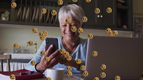 Animation-Von-Emoji-Symbolen-über-Einer-älteren-Frau-Mit-Gemischter-Abstammung,-Die-Ein-Smartphone-Verwendet