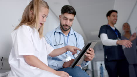 Young-Asian-doctor-reviews-medical-information-on-a-tablet-with-a-Caucasian-girl,-with-copy-space