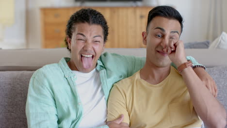 Happy-diverse-gay-male-couple-having-video-call-and-making-funny-faces-at-home,-slow-motion