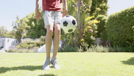 Low-section-of-biracial-man-practicing-skills-with-football-in-sunny-garden,-copy-space,-slow-motion