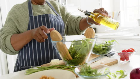 Happy-african-american-senior-woman-mixing-salad-in-sunny-kitchen,-slow-motion