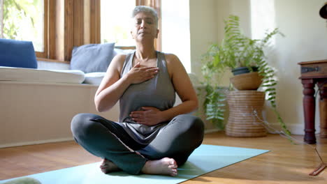 Fokussierte-ältere-Frau-Mit-Gemischter-Abstammung-Meditiert-Zu-Hause-Auf-Yogamatte