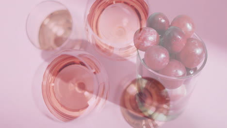 Verbund-Aus-Gläsern-Roséwein-über-Roten-Trauben-Auf-Rosa-Hintergrund