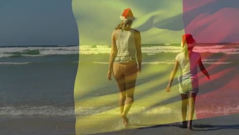 Animation-of-belgian-flag-over-caucasian-mother-and-daughter-in-christmas-hats-on-beach