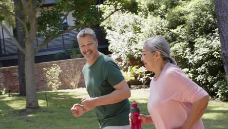 Happy-diverse-senior-couple-running-and-holding-water-bottle-in-sunny-outdoors
