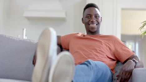 Glücklicher-Afroamerikanischer-Mann,-Der-Im-Sonnigen-Wohnzimmer-Sitzt-Und-Lächelt,-Zeitlupe