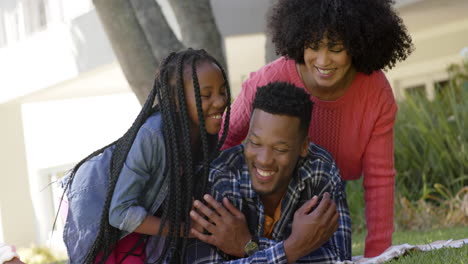 Felices-Padres-Afroamericanos-Con-Su-Hija-Tumbada-Sobre-Una-Manta-En-El-Jardín-De-Casa,-Cámara-Lenta