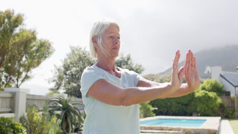 Focused-caucasian-senior-woman-practising-yoga-in-sunny-garden,-slow-motion,-copy-space