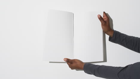 Video-of-hand-of-african-american-man-holding-book-with-blank-pages,-copy-space-on-white-background