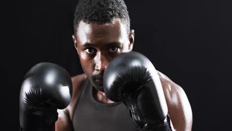 Focused-African-American-boxer-training-in-a-dark-gym-on-a-black-background