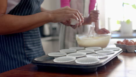 Midsection-of-biracial-mother-and-daughter-making-cup-cakes-in-kitchen,-copy-space,-slow-motion
