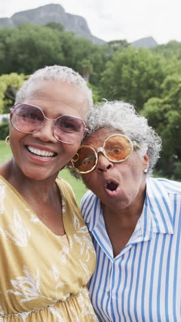 Vertical-video-portrait-of-senior-african-american-female-friends-sticking-out-tongues,-slow-motion