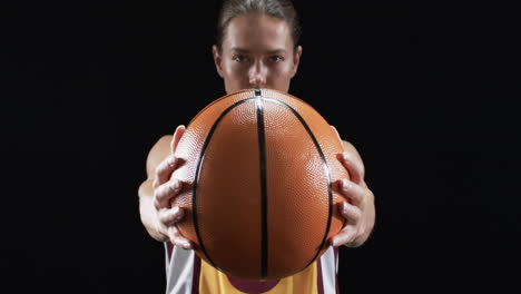 Focused-young-Caucasian-woman-holds-a-basketball-in-front-of-her-on-a-black-background