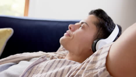 Happy-biracial-man-in-headphones-lying-on-couch,-smiling-with-eyes-closed,-slow-motion