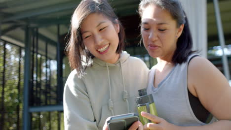 Glückliche-Asiatische-Freundinnen-Mit-Wasserflasche-Und-Smartphone-Lachen-Auf-Der-Terrasse,-Zeitlupe