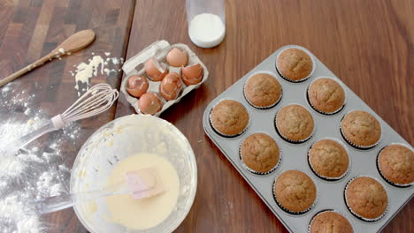 Freshly-baked-cupcakes,-mixing-bowl,-utensils-and-used-ingredients-on-kitchen-worktop,-slow-motion