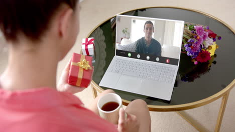 Caucasian-man-holding-gift-and-talking-with-caucaslan-woman-on-laptop-screen