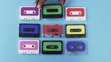 Video-of-african-american-man's-hand-arranging-retro-tapes-with-copy-space-on-blue-background
