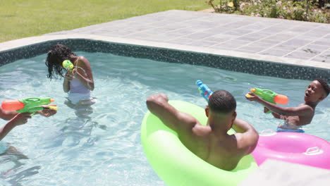 Happy-african-american-parents,-son-and-daughter-playing-with-water-pistols-in-pool,-slow-motion