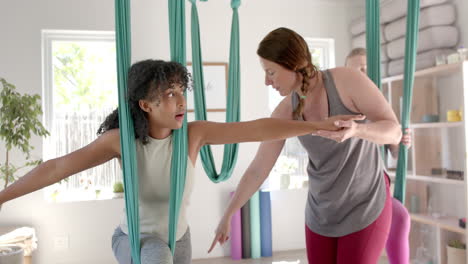 Focused-diverse-fitness-teenage-girl-exercising-in-aerial-yoga-class-and-female-coach,-slow-motion