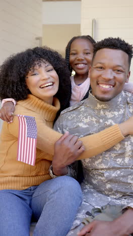 Vertical-video-of-portrait-of-happy-african-american-male-soldier-with-family-at-home,-slow-motion