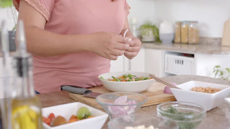 Midsection-of-plus-size-biracial-woman-making-meal-with-vegetables-in-kitchen,-slow-motion