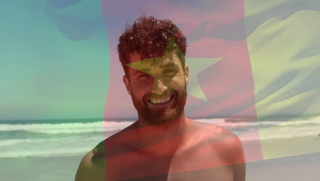 Animation-of-flag-of-cameroon-over-happy-caucasian-man-smiling-on-sunny-beach