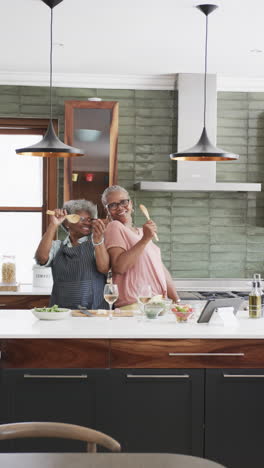 Vertical-video-of-senior-african-american-female-friends-singing-in-kitchen,-copy-space,-slow-motion