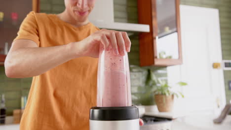 Happy-biracial-man-preparing-fruit-smoothie-with-blender-in-kitchen,-copy-space,-slow-motion