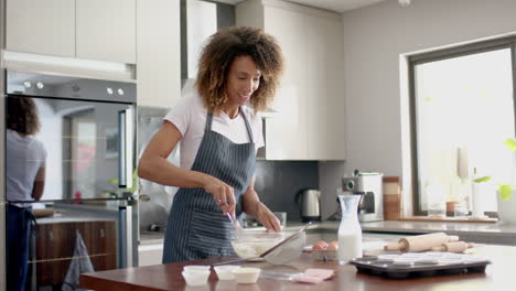 Happy-biracial-woman-in-apron-mixing-cake-mix,-baking-in-kitchen,-copy-space,-slow-motion