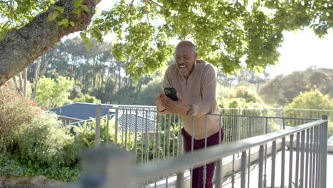 Happy-senior-biracial-man-using-smartphone-at-balcony-at-home,-slow-motion