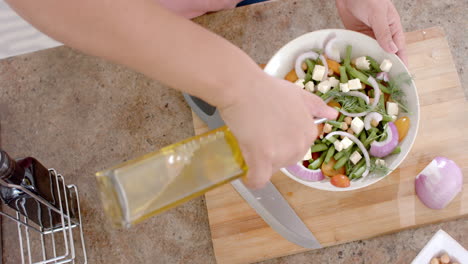 Hands-of-biracial-woman-dressing-salad-with-olive-oil-in-kitchen,-copy-space,-slow-motion