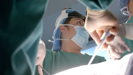 Biracial-female-surgeon-using-using-headlight-and-surgical-tools-during-operation,-slow-motion