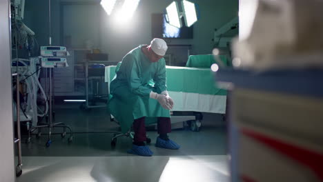 Caucasian-male-surgeon-wearing-surgical-gown-sitting-in-operating-theatre-at-hospital,-slow-motion