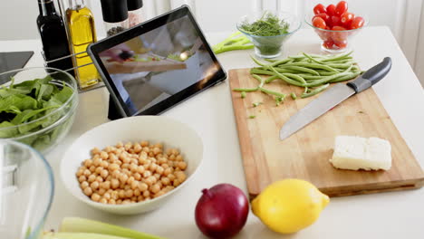 Knife,-cutting-board,-vegetables-and-tablet-on-counter-in-sunny-kitchen,-slow-motion